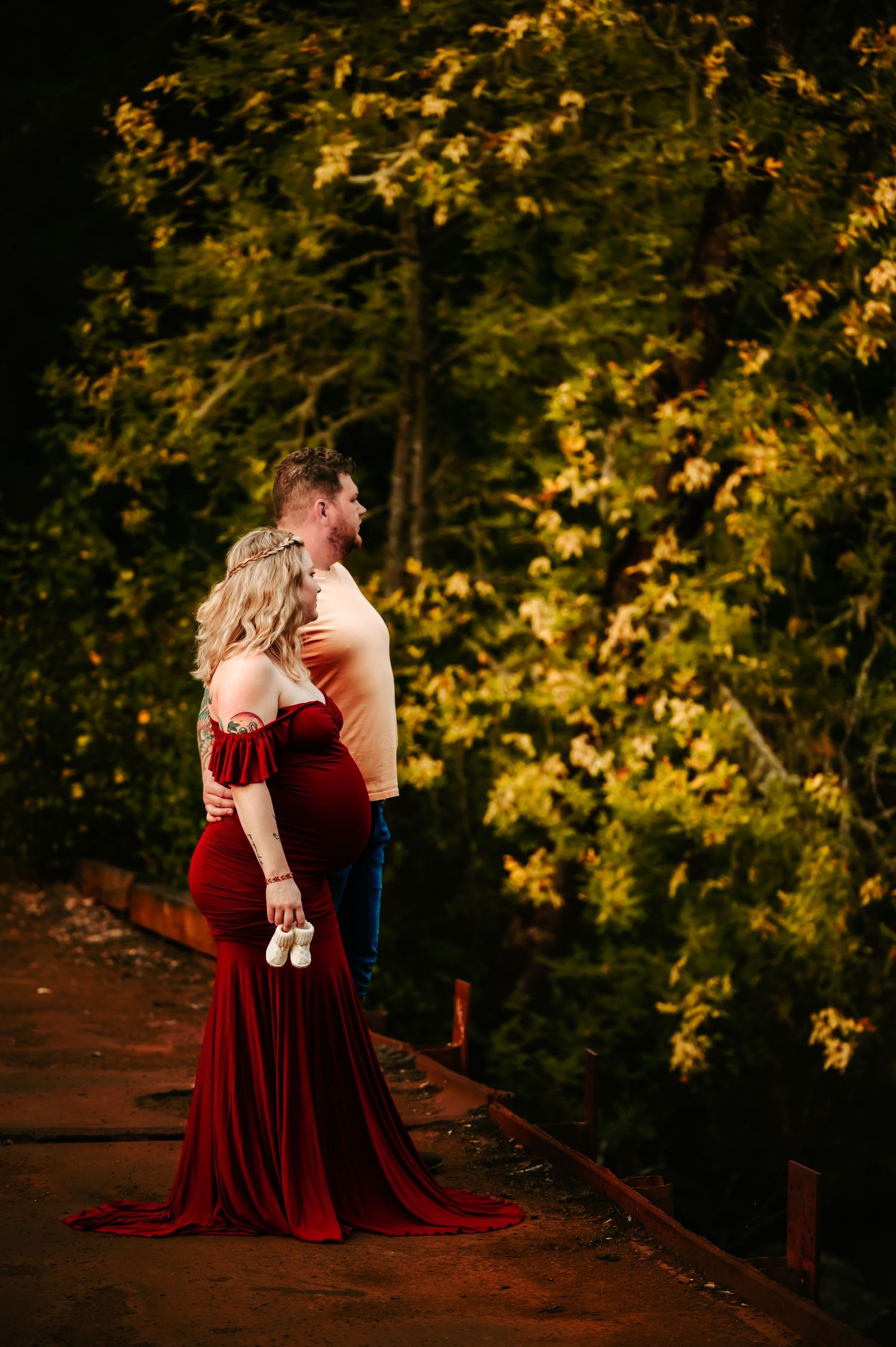 Couple embraces on wooden bridge surrounded by golden autumn trees.