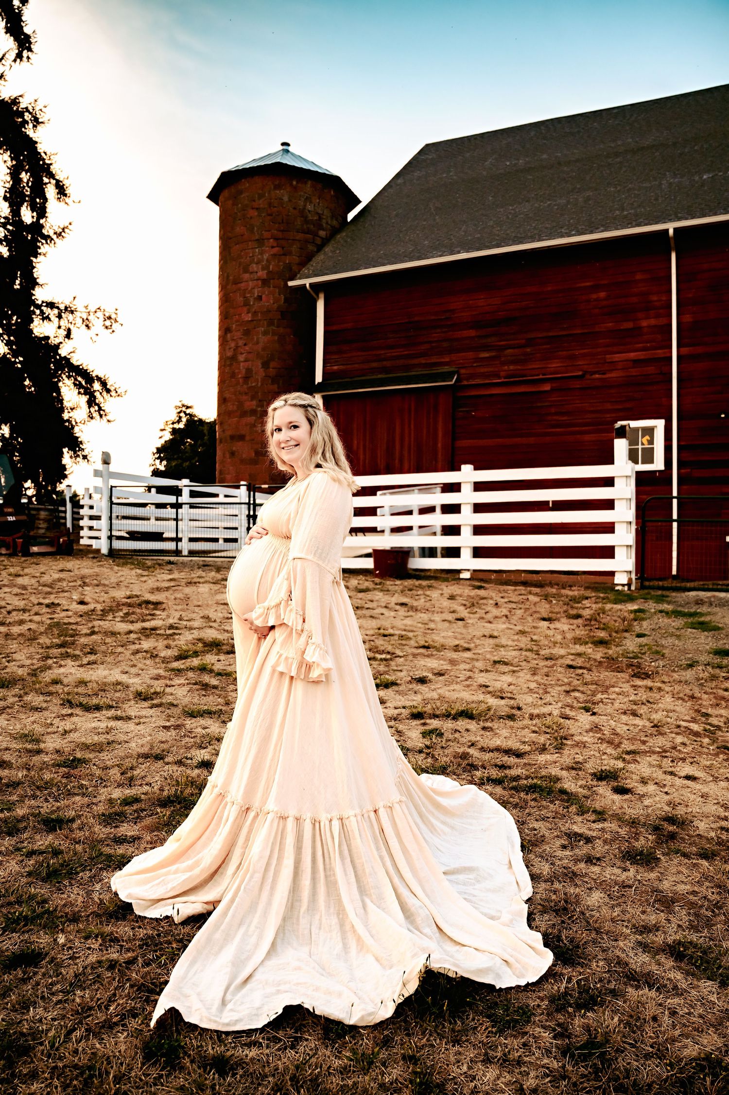 Ethereal dress photography session near a classic red barn with white fencing at sunset.