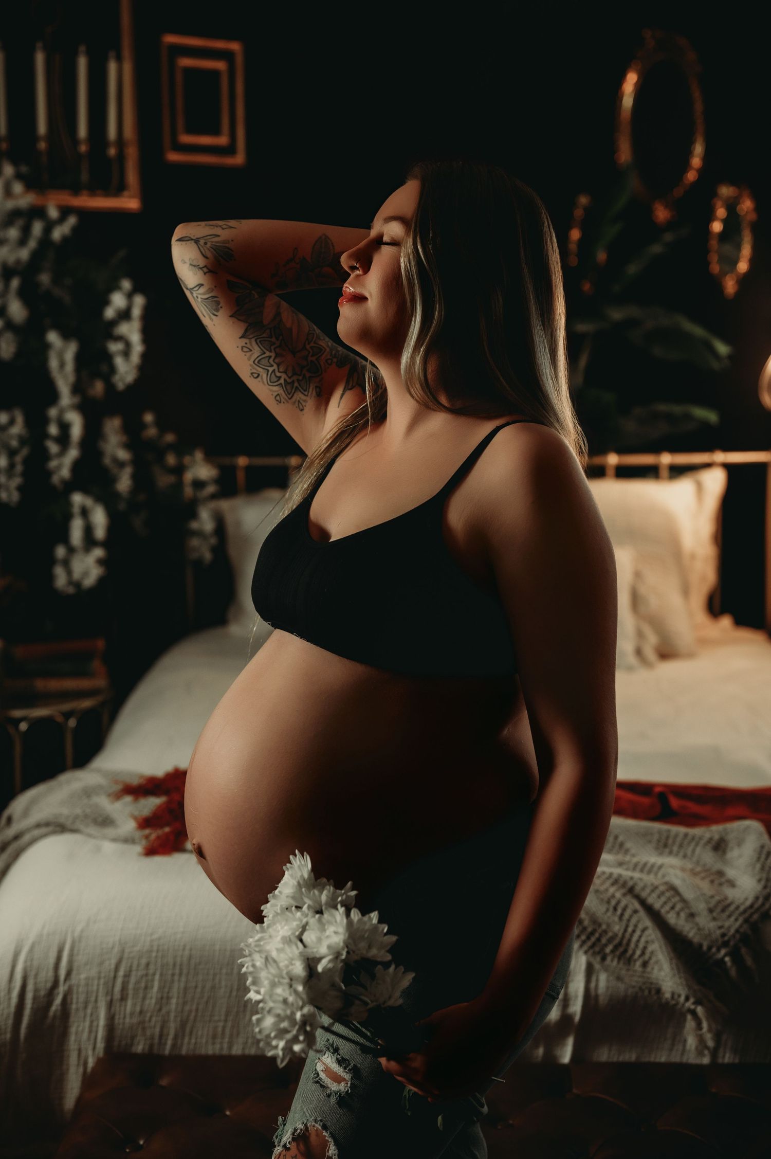 Intimate maternity portrait with moody lighting and white flowers against dark background.