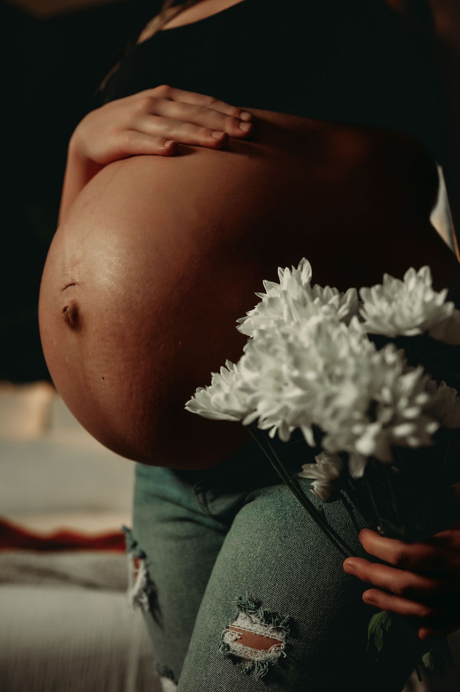 Close-up maternity photo showing white flowers against distressed denim.