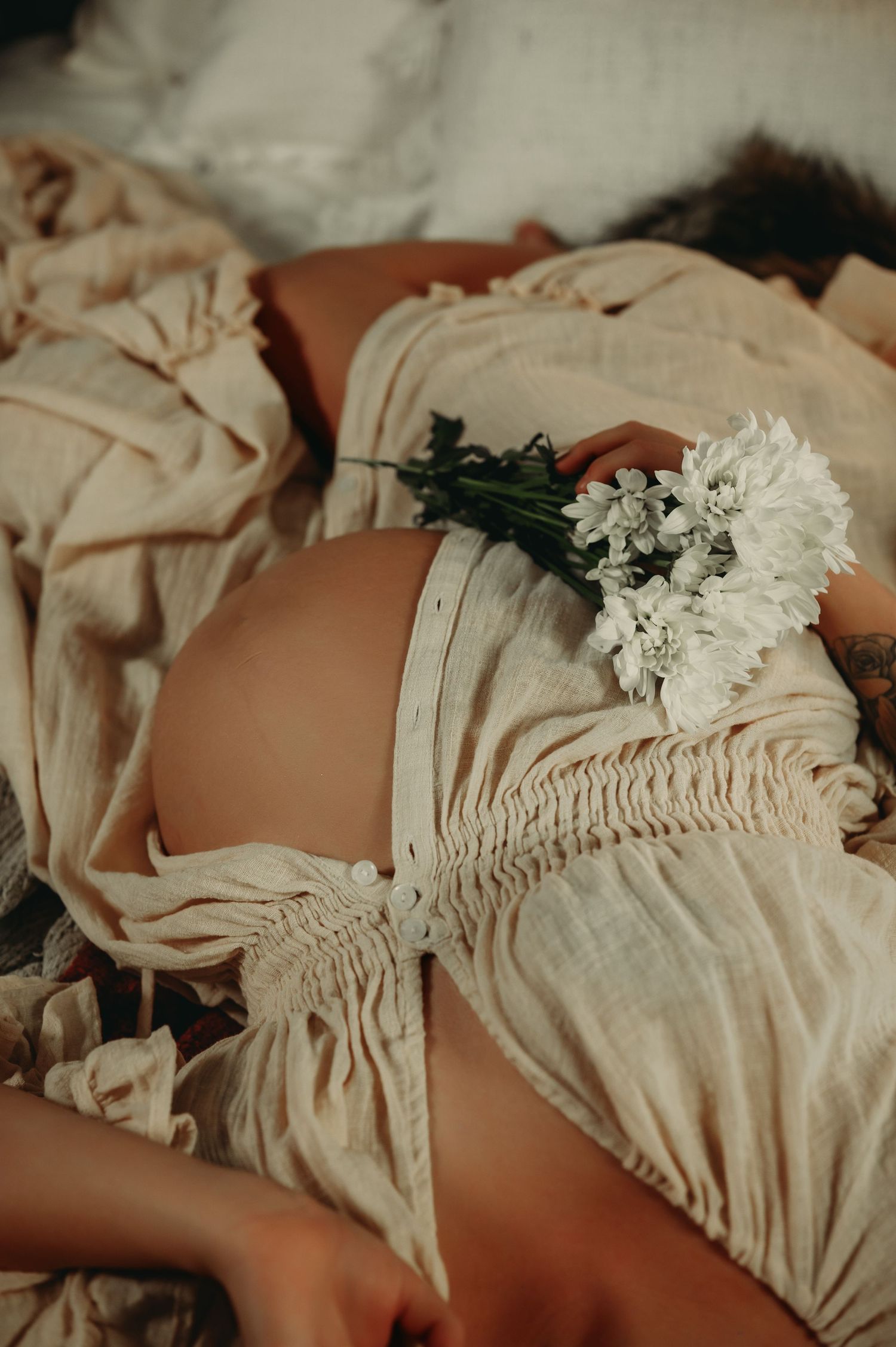 Artistic maternity photo featuring cream-colored ruched fabric and white floral accents.
