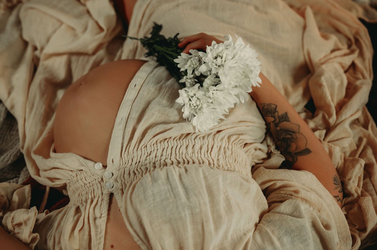 Detail shot of gathered fabric and white flowers in maternity photography.