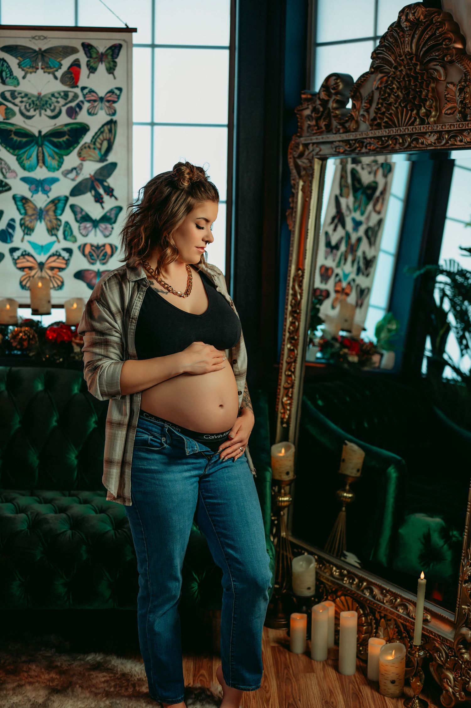 Artistic maternity photo against butterfly wallpaper in moody lighting.