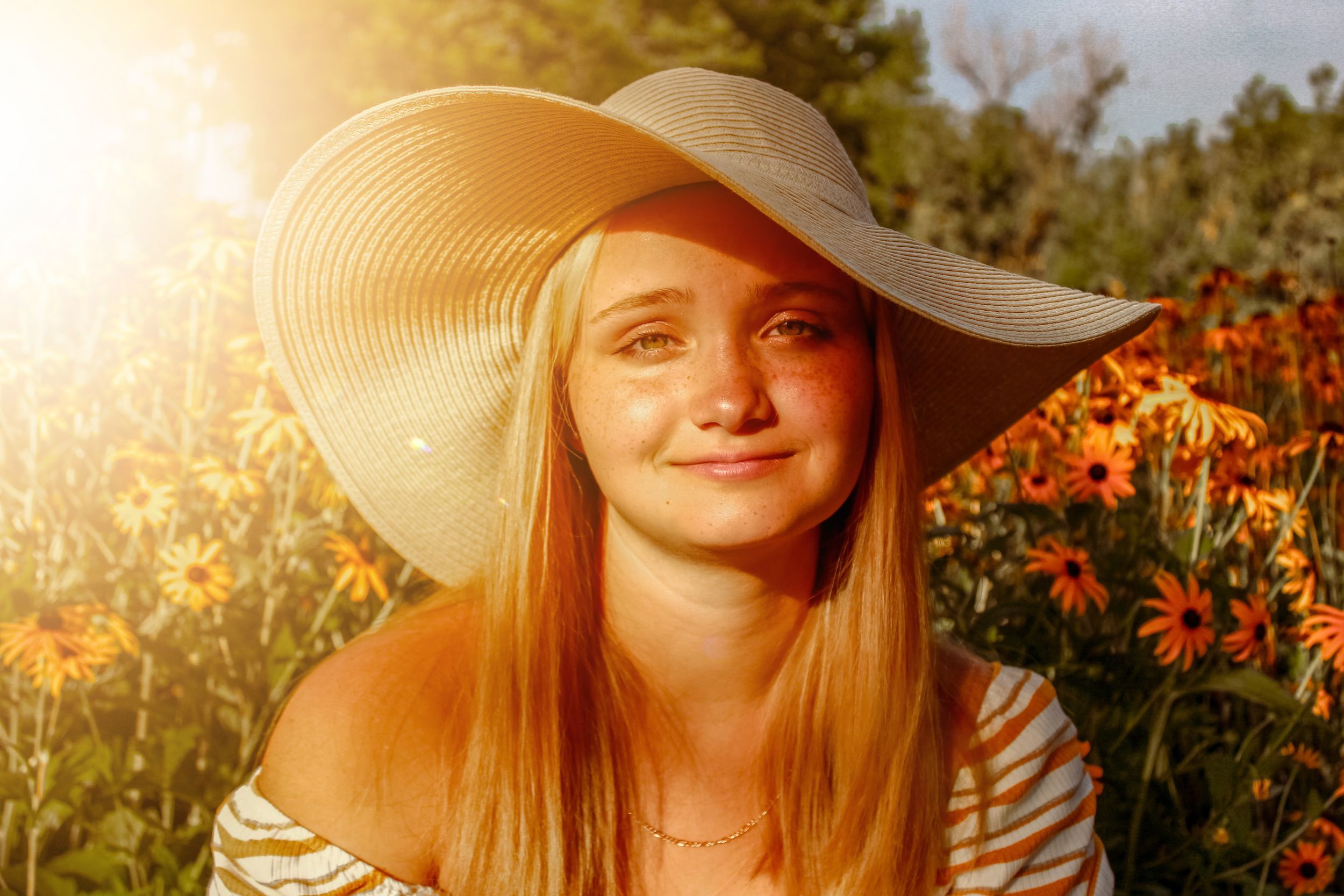 Woman in sunhat sitting among orange flowers at sunset with warm golden light.
