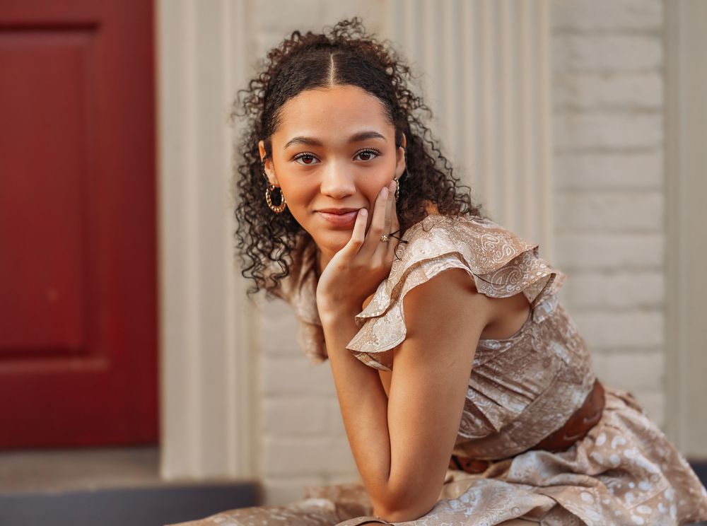 Woman in floral vintage-style dress with ruffled sleeves leans on elbows while smiling warmly at camera.