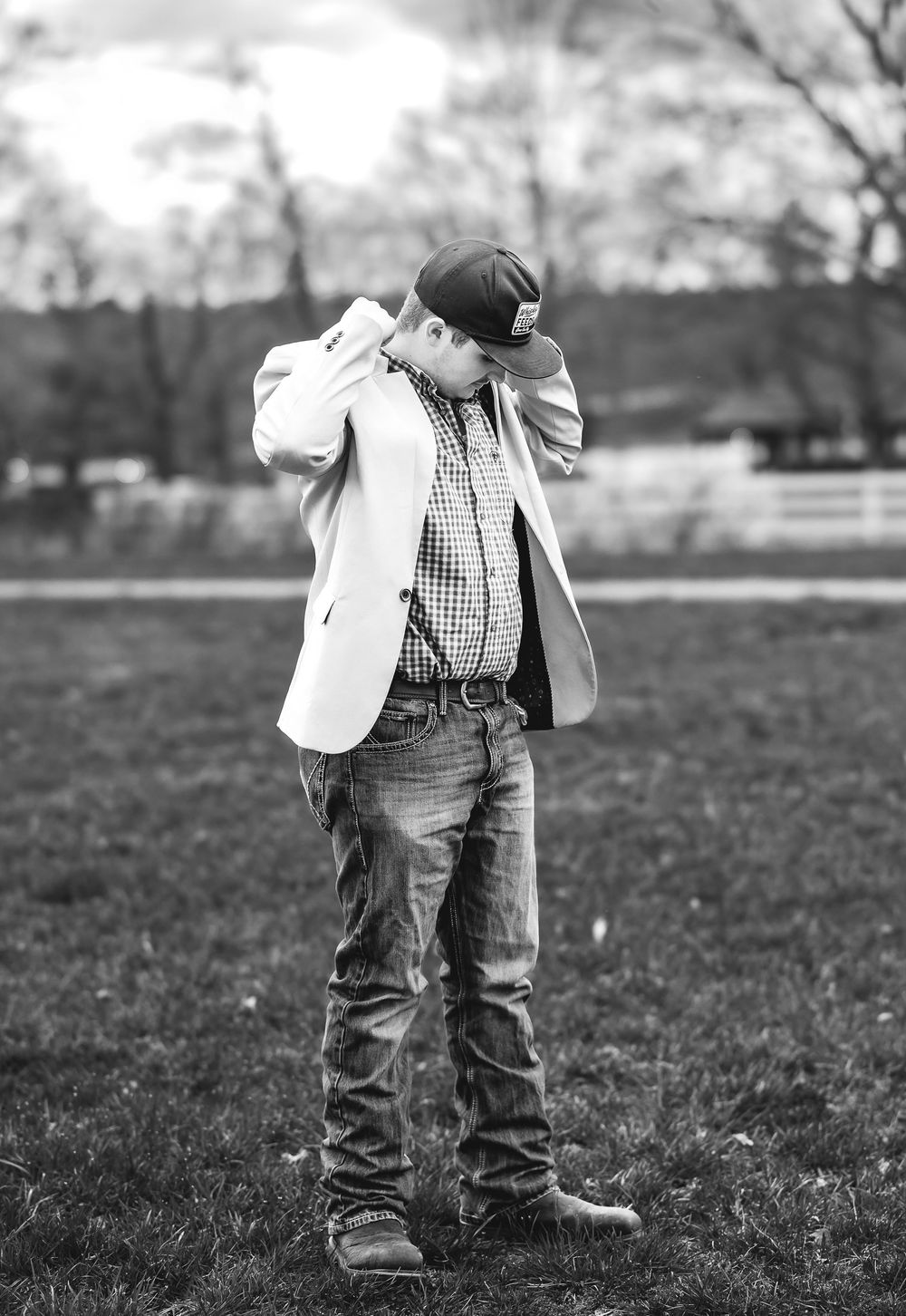 A young child in a white blazer and jeans walks through a grassy field in black and white photography.
