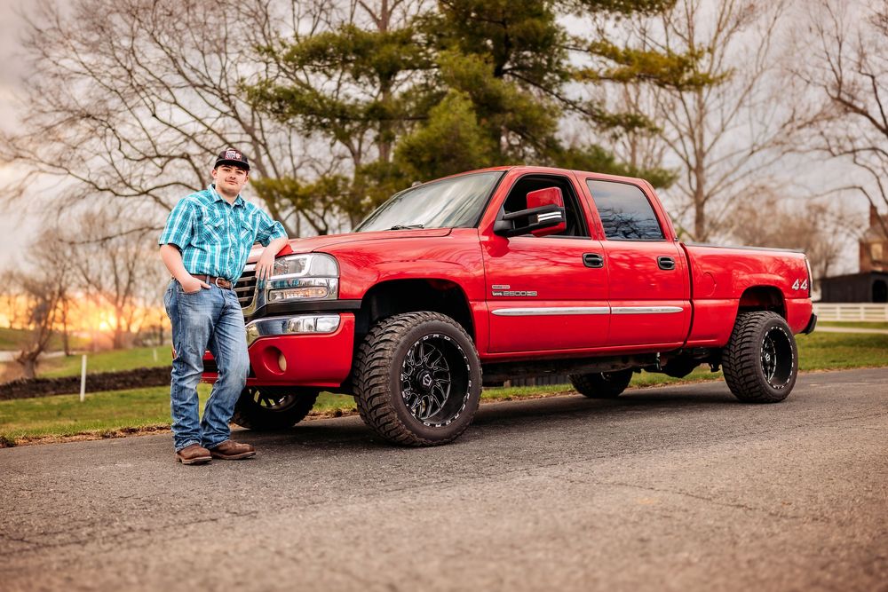 A red lifted Chevrolet Silverado pickup truck with black wheels parked on a gravel road next to trees.