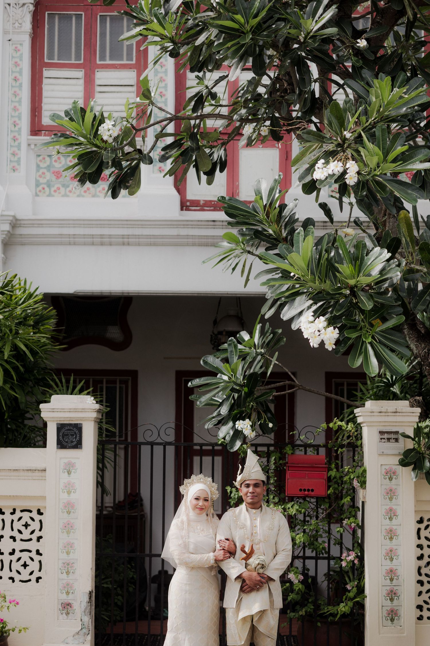 Couple in traditional dress posing along vintage shophouses with ornate architecture.
