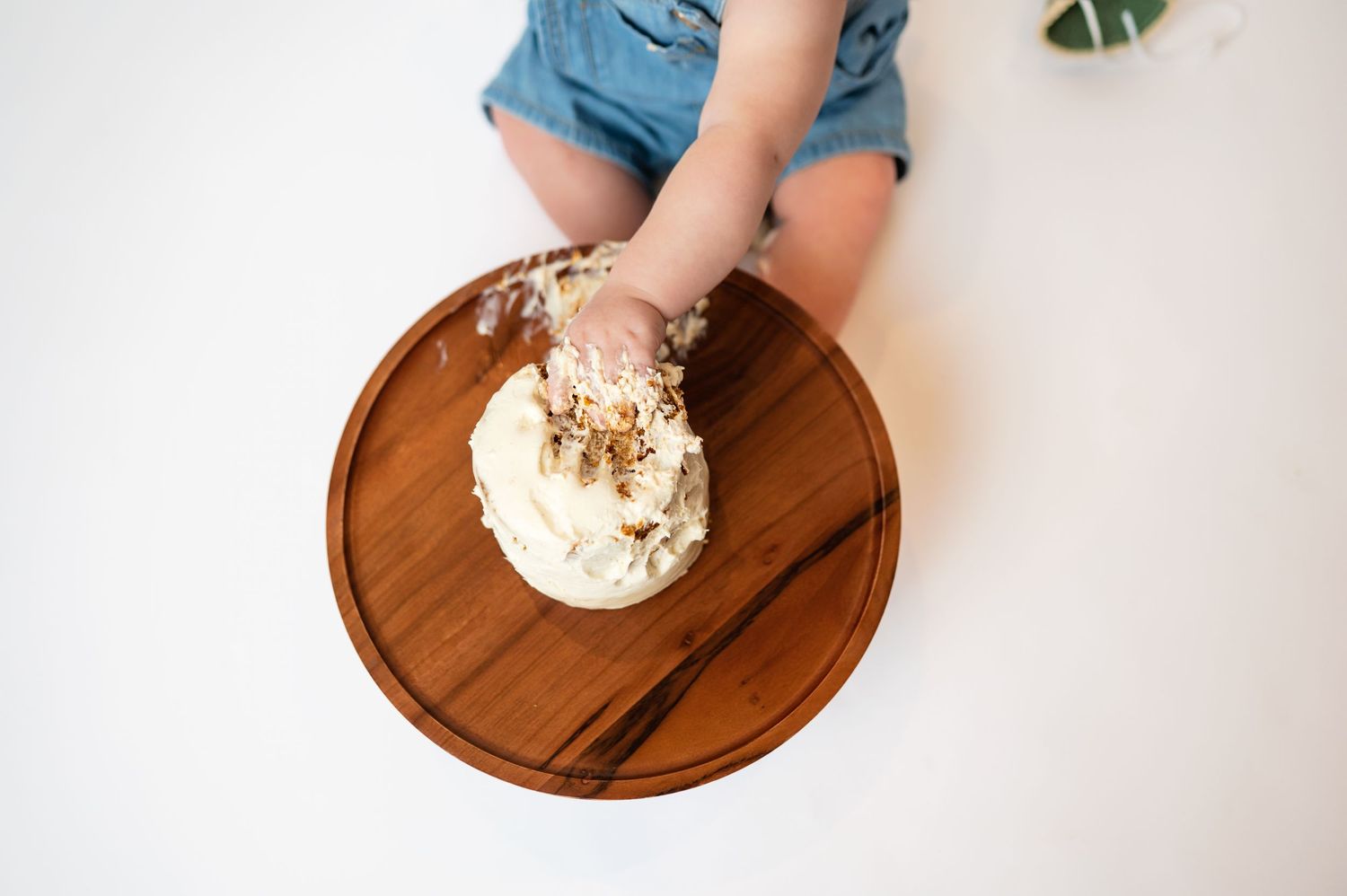 aerial view of vanilla iced cake with 12-month old's hand grabbing chunk from the top