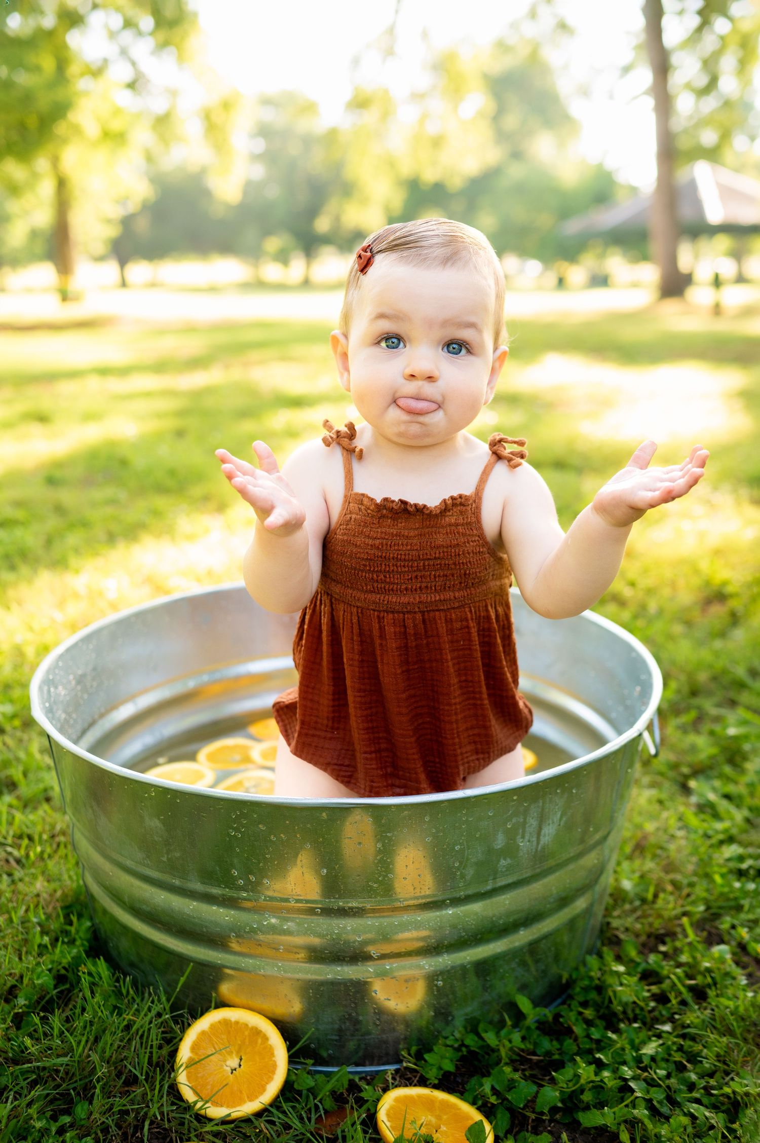 1 year old sunny outdoors in large galvanized bucket filled with water and orange slices; standing in bucket with tongue out looking @camera