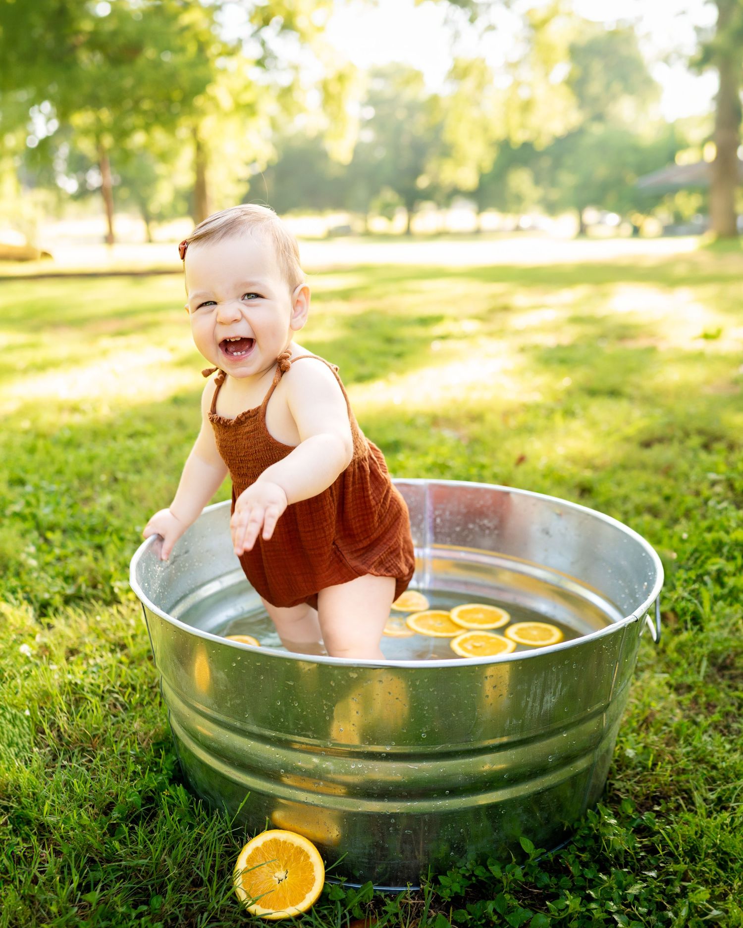1 year old sunny outdoors in large galvanized bucket filled with water and orange slices during 12-month milestone session in waxahachie