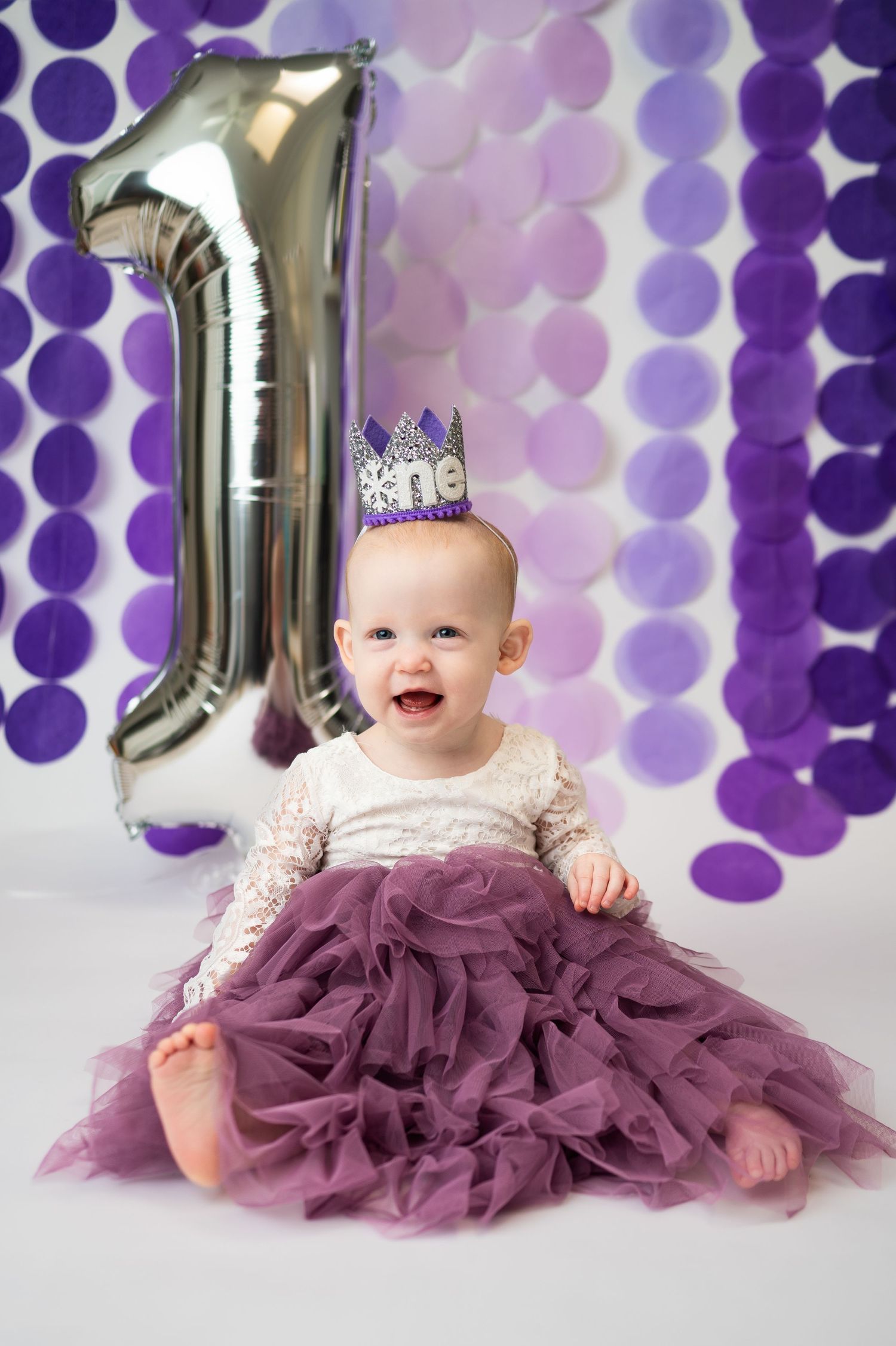 girl smiles in purple tulle skirt wearing crown for dallas area one year cakes mash milestone photos in-home