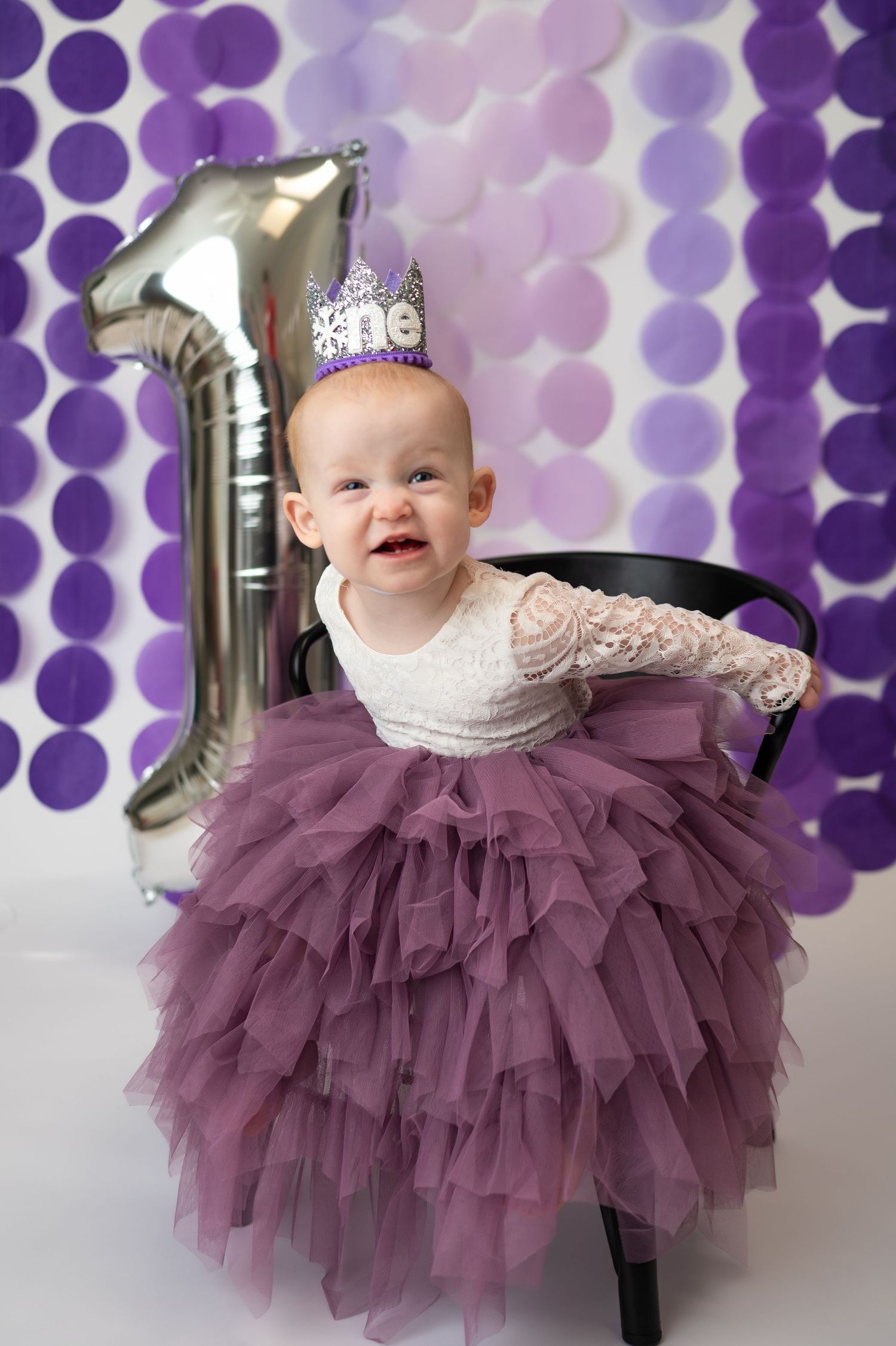 girl smiles in purple tulle skirt wearing crown for dallas area one year cakes mash milestone photos in-home