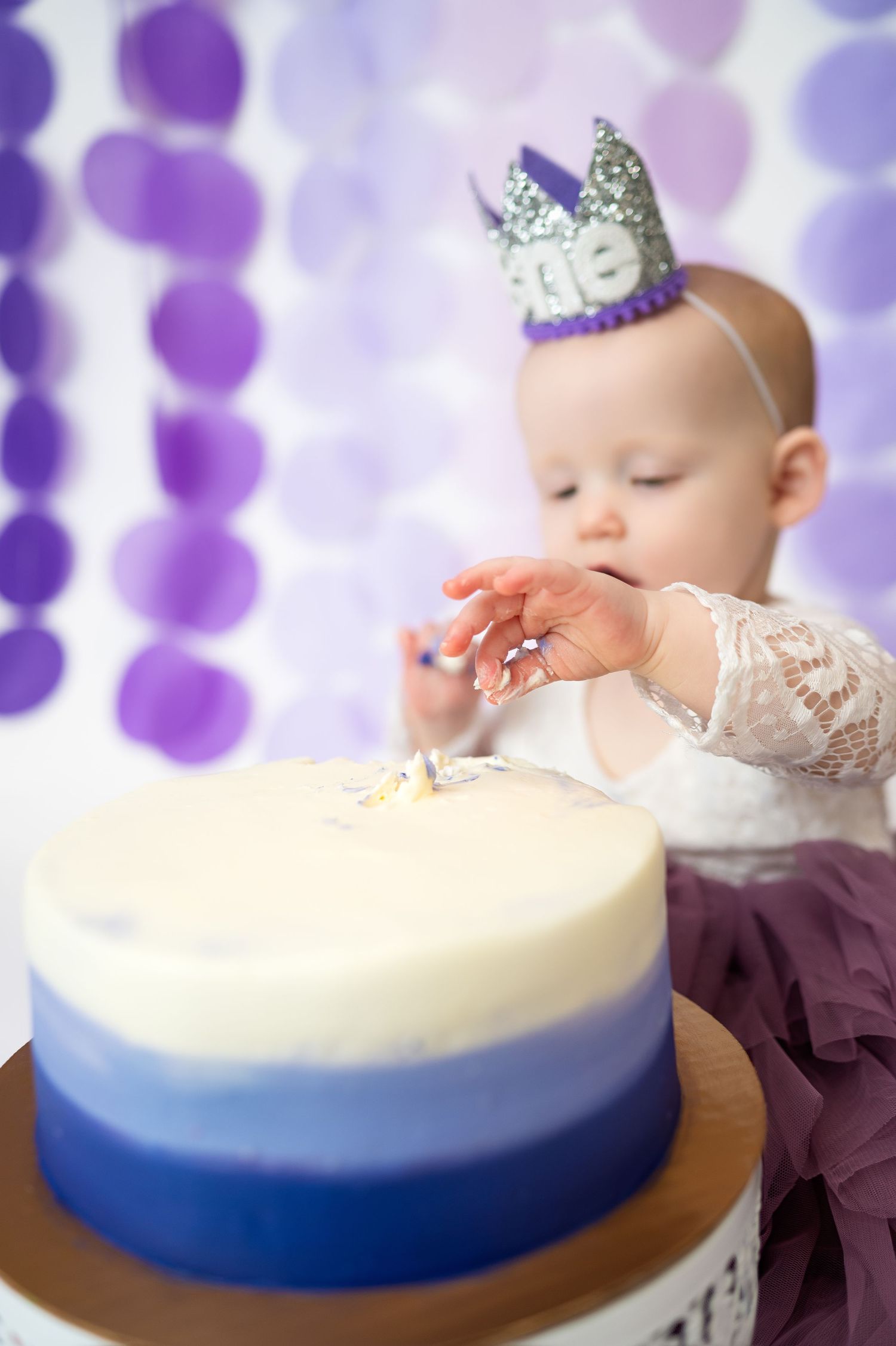 girl reaches into icing of cake during dallas area one year cake smash milestone in-home photo session