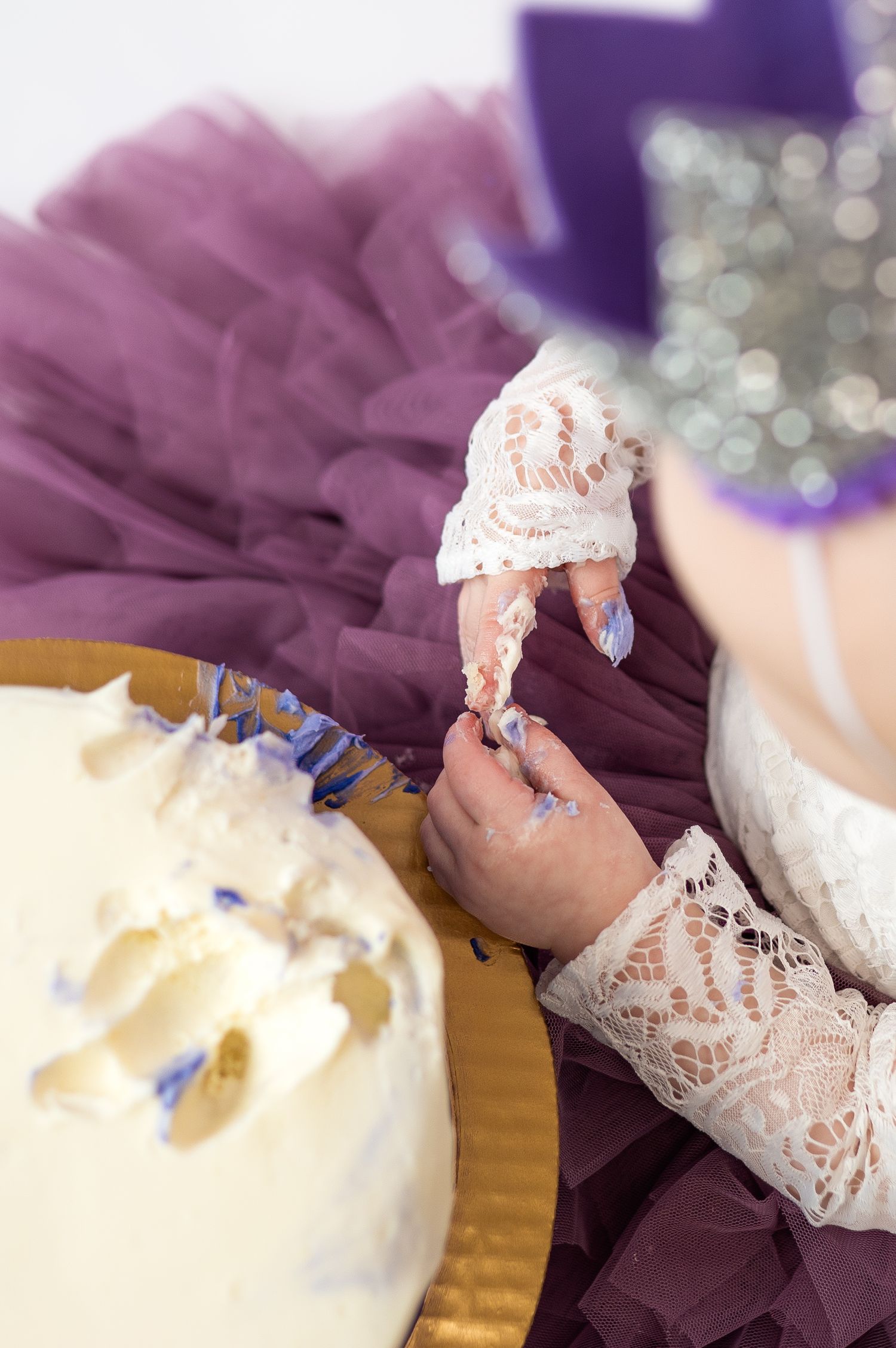 girl reaches into icing of cake during dallas area one year cake smash milestone in-home photo session