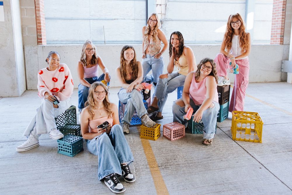 Group of nine young women posing together in a parking garage with colorful milk crates.