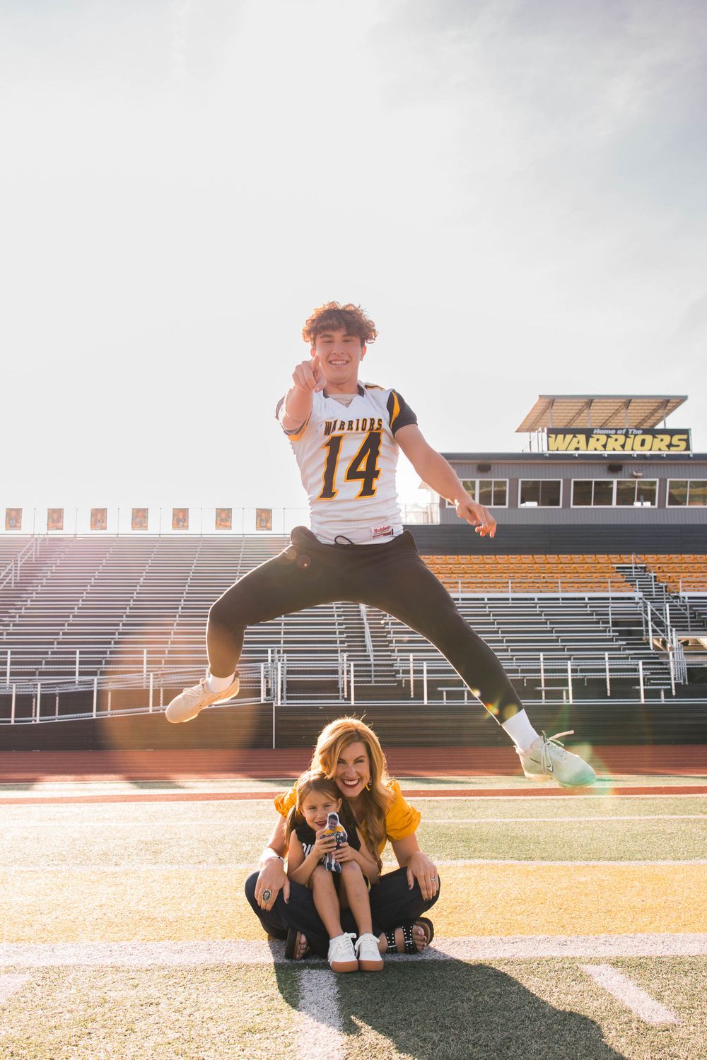 Athletes pose playfully on football field at sunset with stadium bleachers in background.