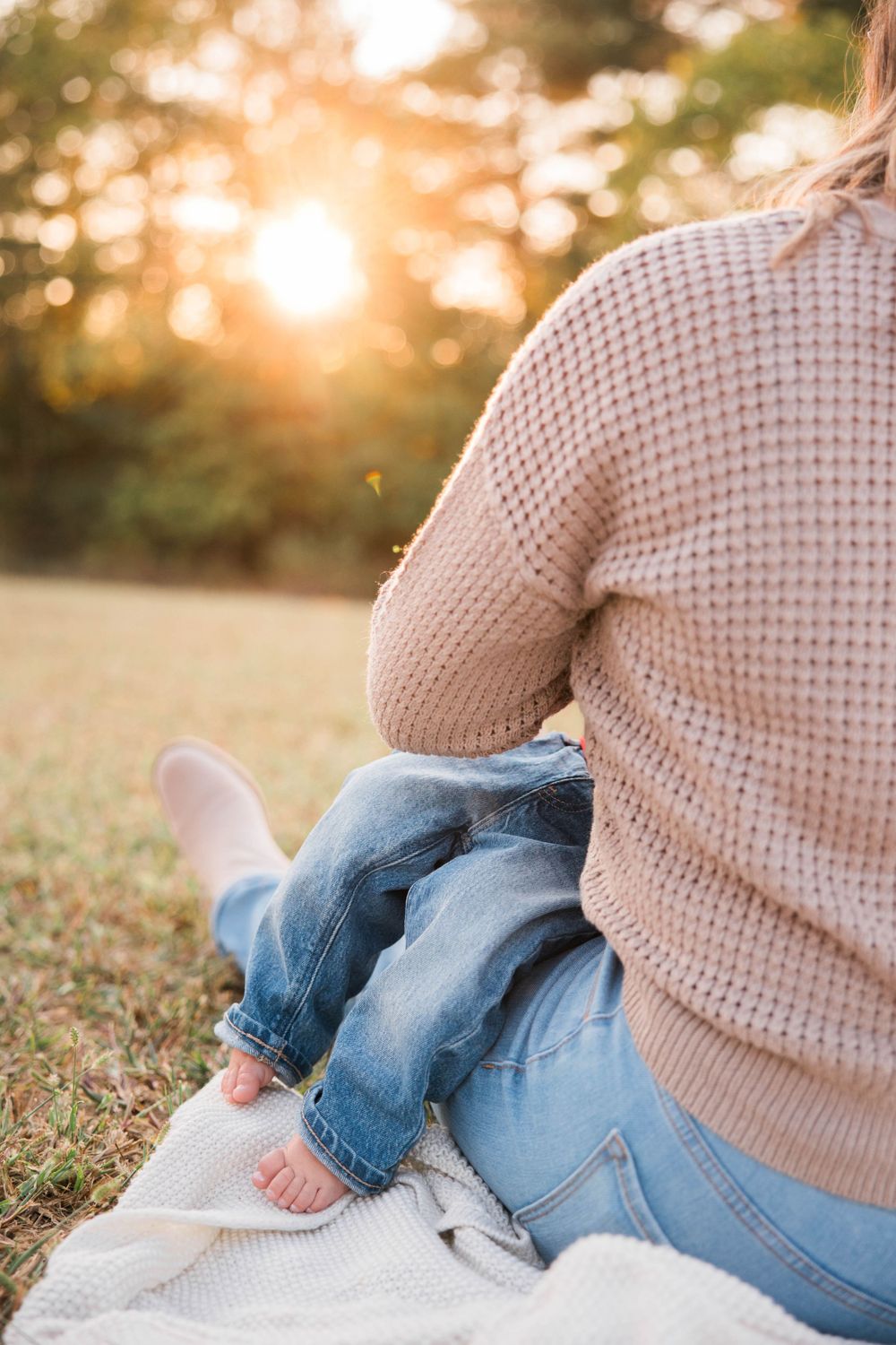 Person in knit sweater sitting on blanket in field during golden sunset.