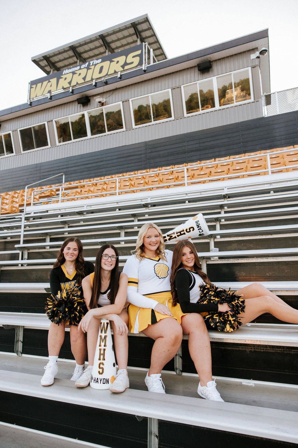 Cheerleaders in black and gold uniforms sit on metal bleachers in a series of candid poses at a sports stadium.