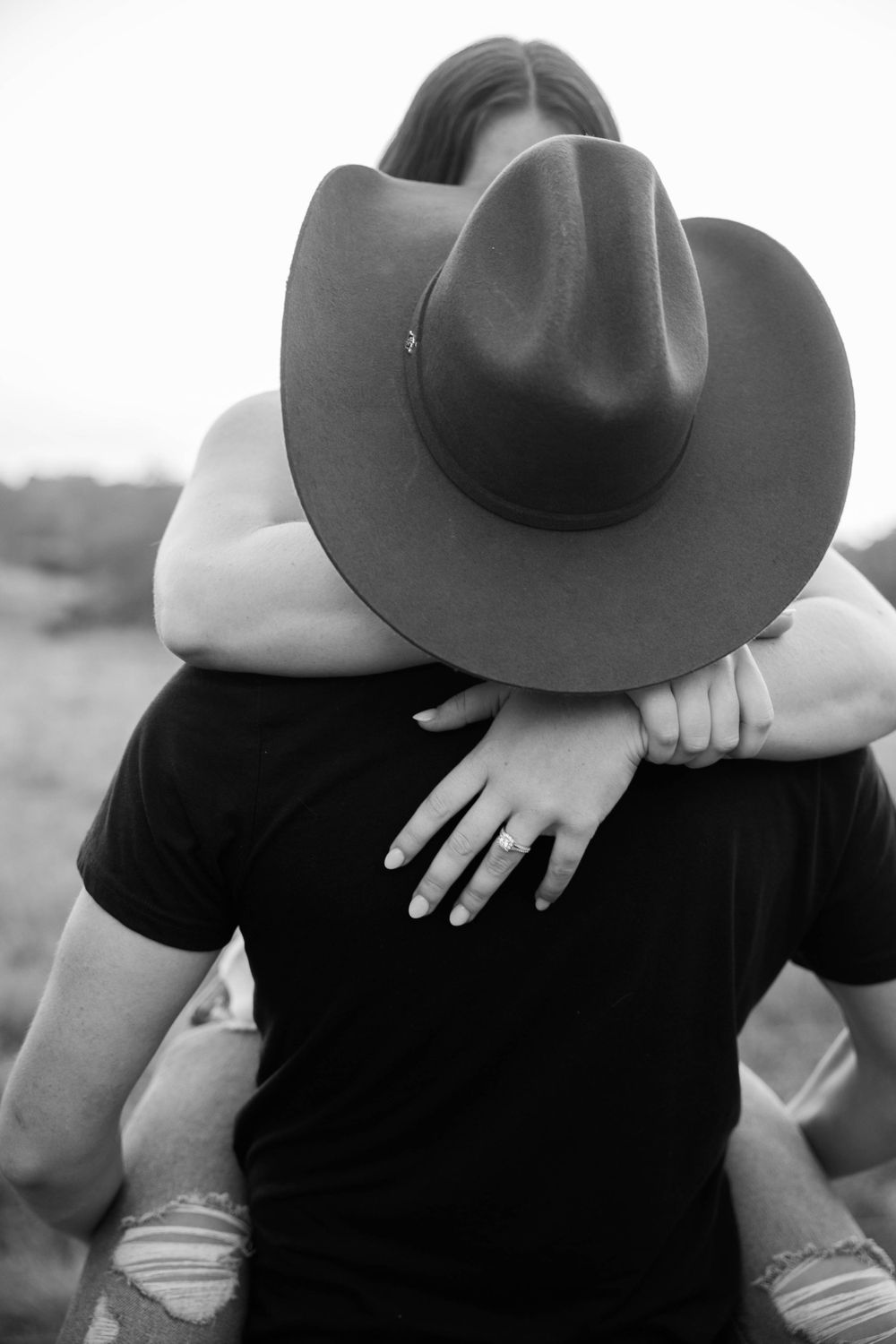 Black and white portrait showing embrace with cowboy hat and engagement ring visible.