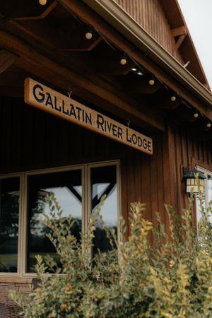 Close up of the Gallatin River Lodge wooden sign on rustic brown building exterior.