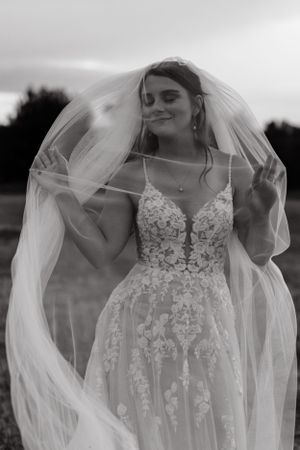 An ethereal bridal portrait featuring a lace wedding dress and flowing veil against a moody sky.
