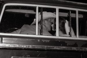 A vintage black and white photograph showing people inside an old car.