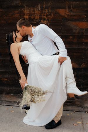 Romantic dip pose against rustic wooden wall with dried flower bouquet.