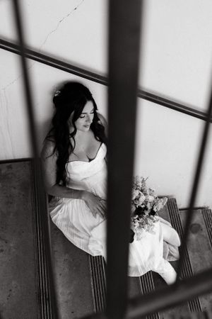 Black and white artistic photo of a bride sitting on stairs with a bouquet.
