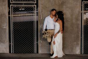 Wedding couple posing against industrial backdrop with chain link fence and concrete walls.