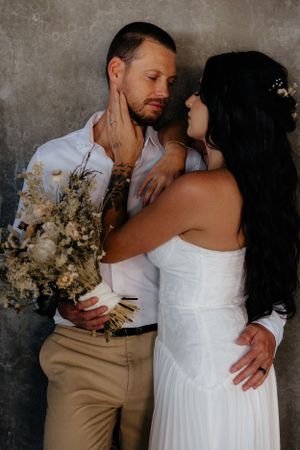Intimate portrait of a couple in wedding attire sharing a tender moment against a concrete wall.