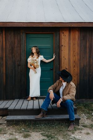 Rustic wedding photo of couple by wooden cabin with teal door.