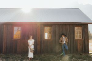 Artistic wedding photo against a rustic wooden cabin with sun flare.