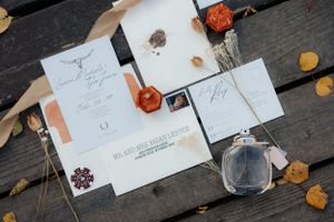 Wedding stationery flat lay with fall leaves and perfume bottle on wooden surface.