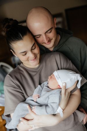 A tender moment between parents and their newborn baby in matching gray sweaters, captured in a series of intimate photos.