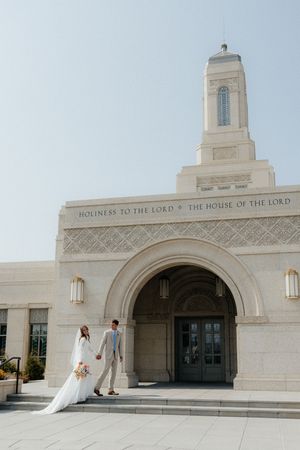 Panoramic view of a white stone Mormon temple entrance with arched doorways and 'House of the Lord' inscription.