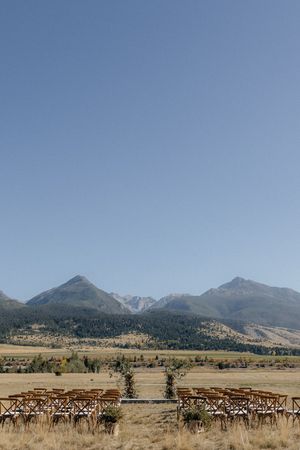Wooden chairs arranged outdoors for a ceremony with scenic mountain peaks and rolling meadows in the background.
