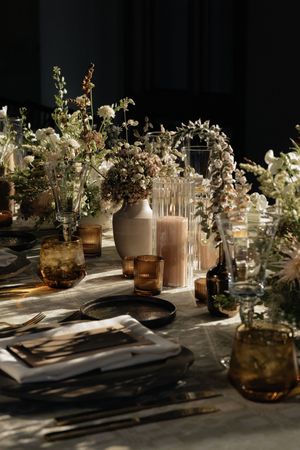 Elegant table setting with amber glass vases and white floral arrangements creating dramatic shadows in moody lighting.