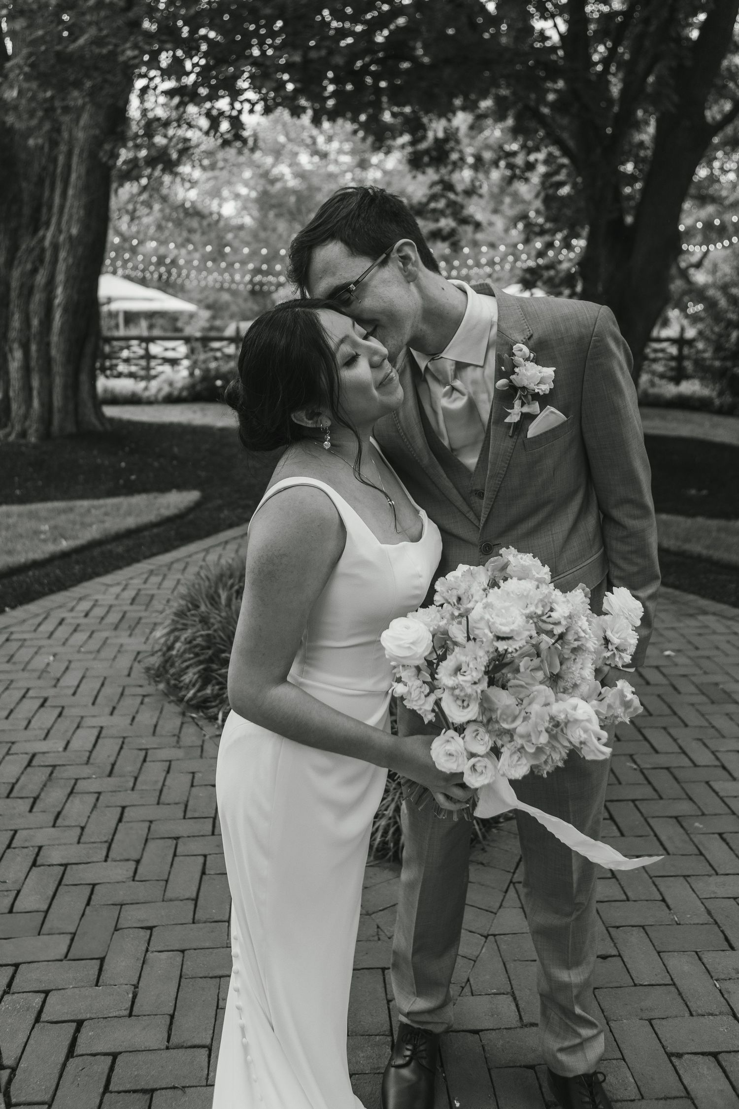 A wedding couple poses against a brick wall with dramatic window light and vintage sofa.