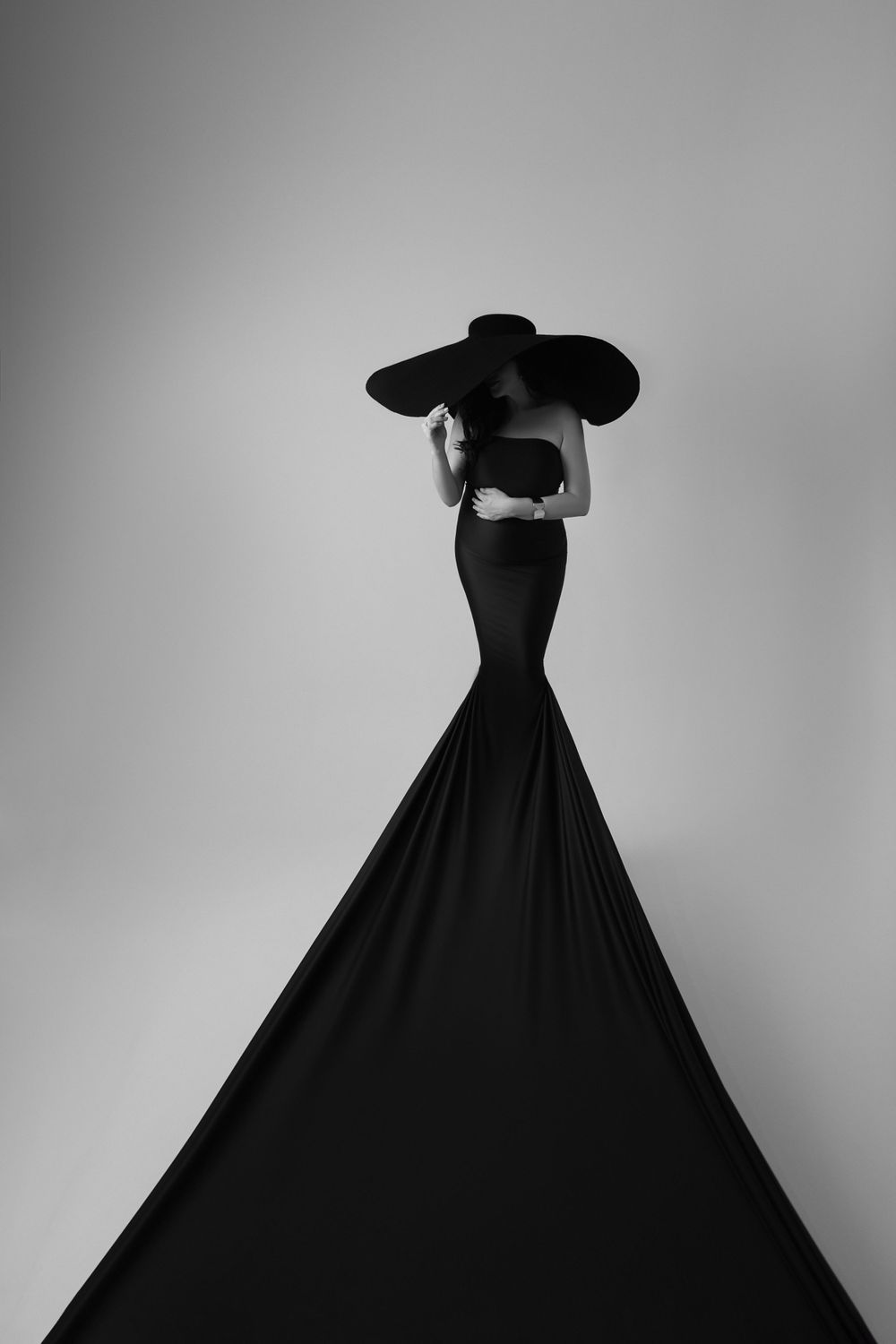 Artistic black and white silhouette of woman in dramatic flowing gown with wide hat.