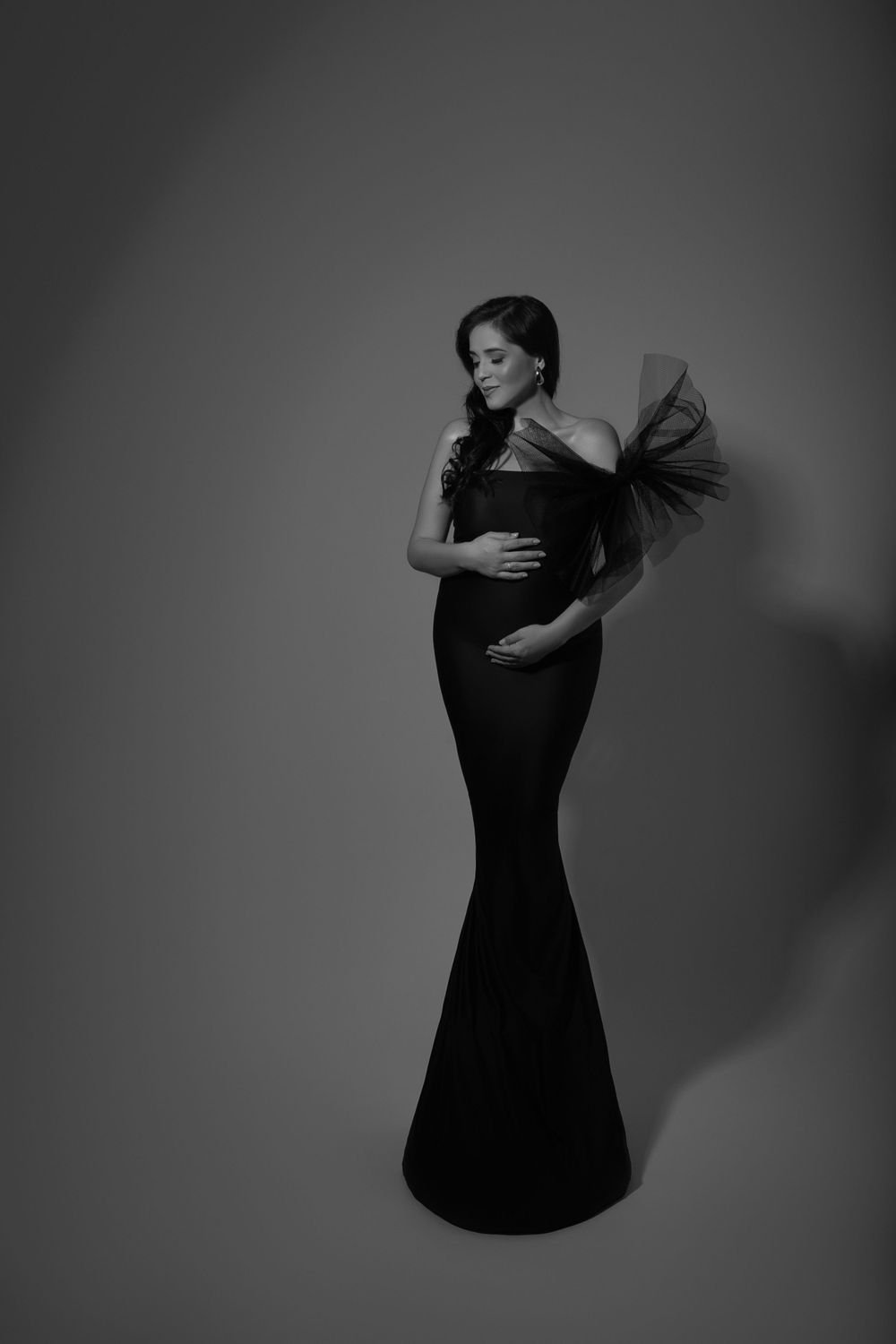 Dramatic black evening gown maternity photo featuring a flowing mermaid silhouette with voluminous tulle shoulder detail.