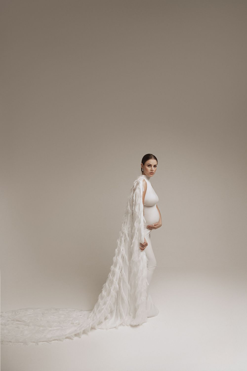 Elegant maternity photo featuring white gown with dramatic textured cape.