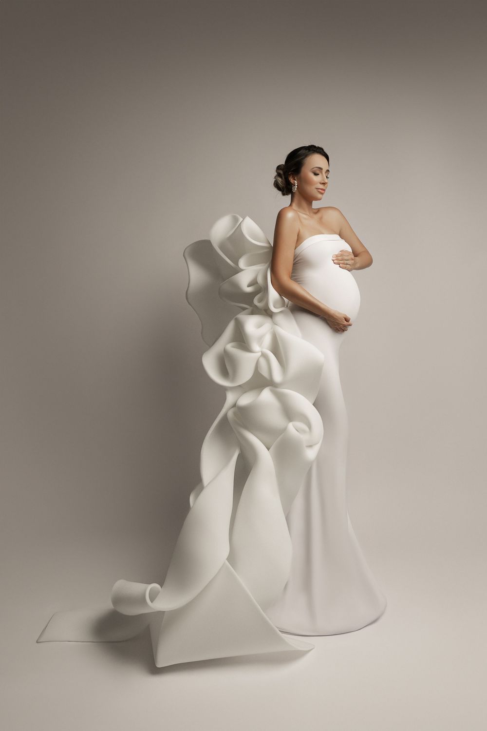 Ethereal maternity portrait in white sculptural gown with dramatic ruffled train detail.