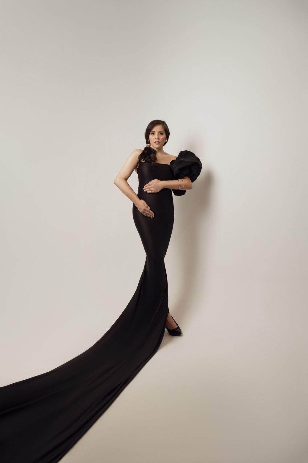 Stunning maternity photo featuring long black mermaid dress with dramatic train against white backdrop.