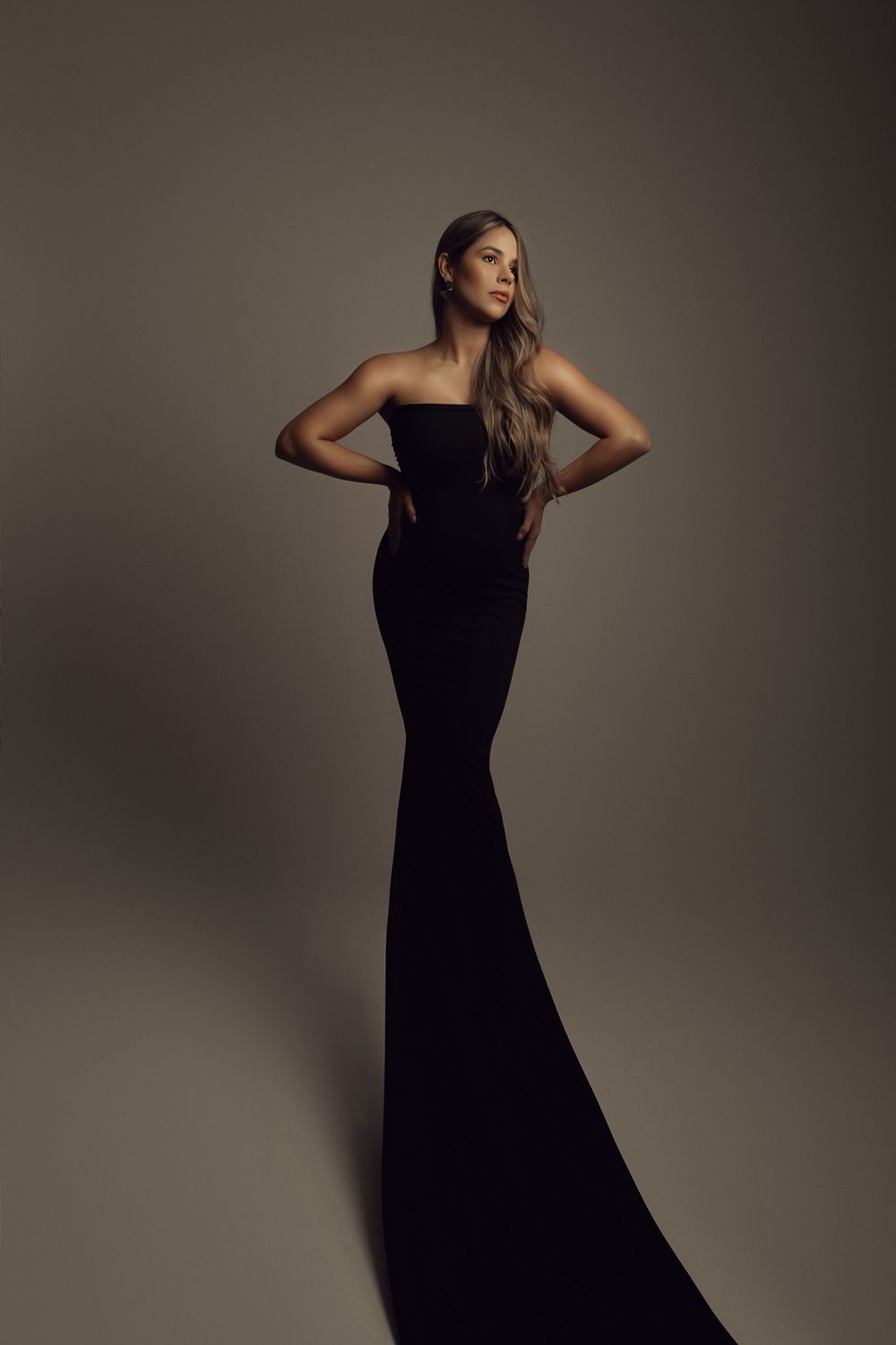 Fashion-forward maternity photo in fitted black evening gown against neutral backdrop.