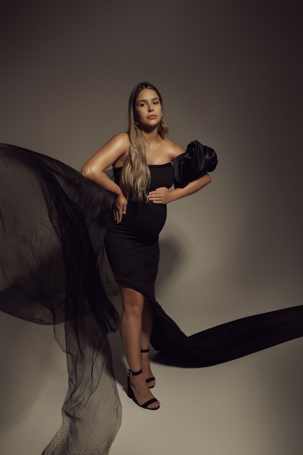 Stylish maternity photo with black dress and flowing fabric creating dynamic movement.