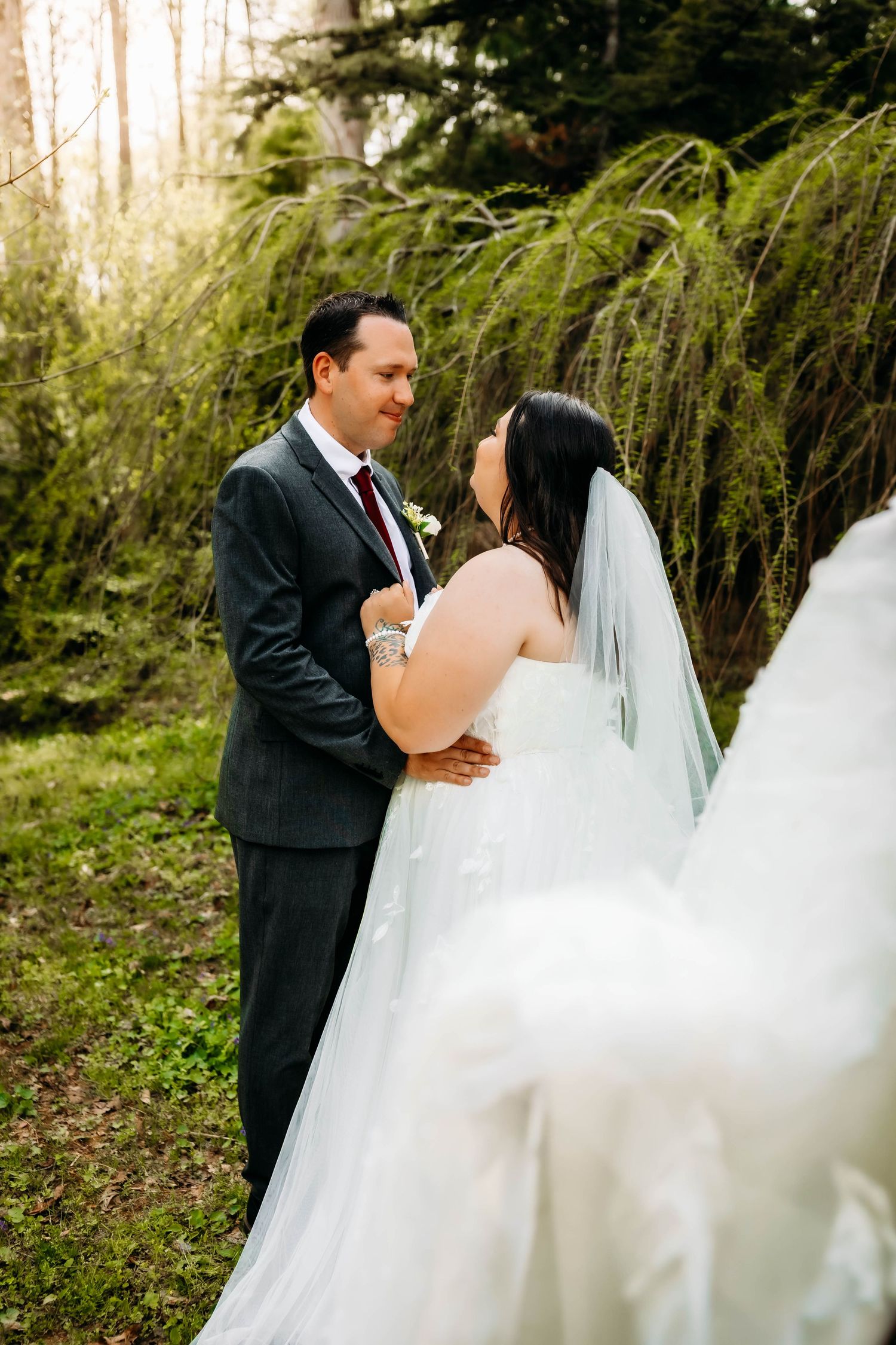 Bride in flowing lace dress holding bouquet during sunset forest wedding photo.
