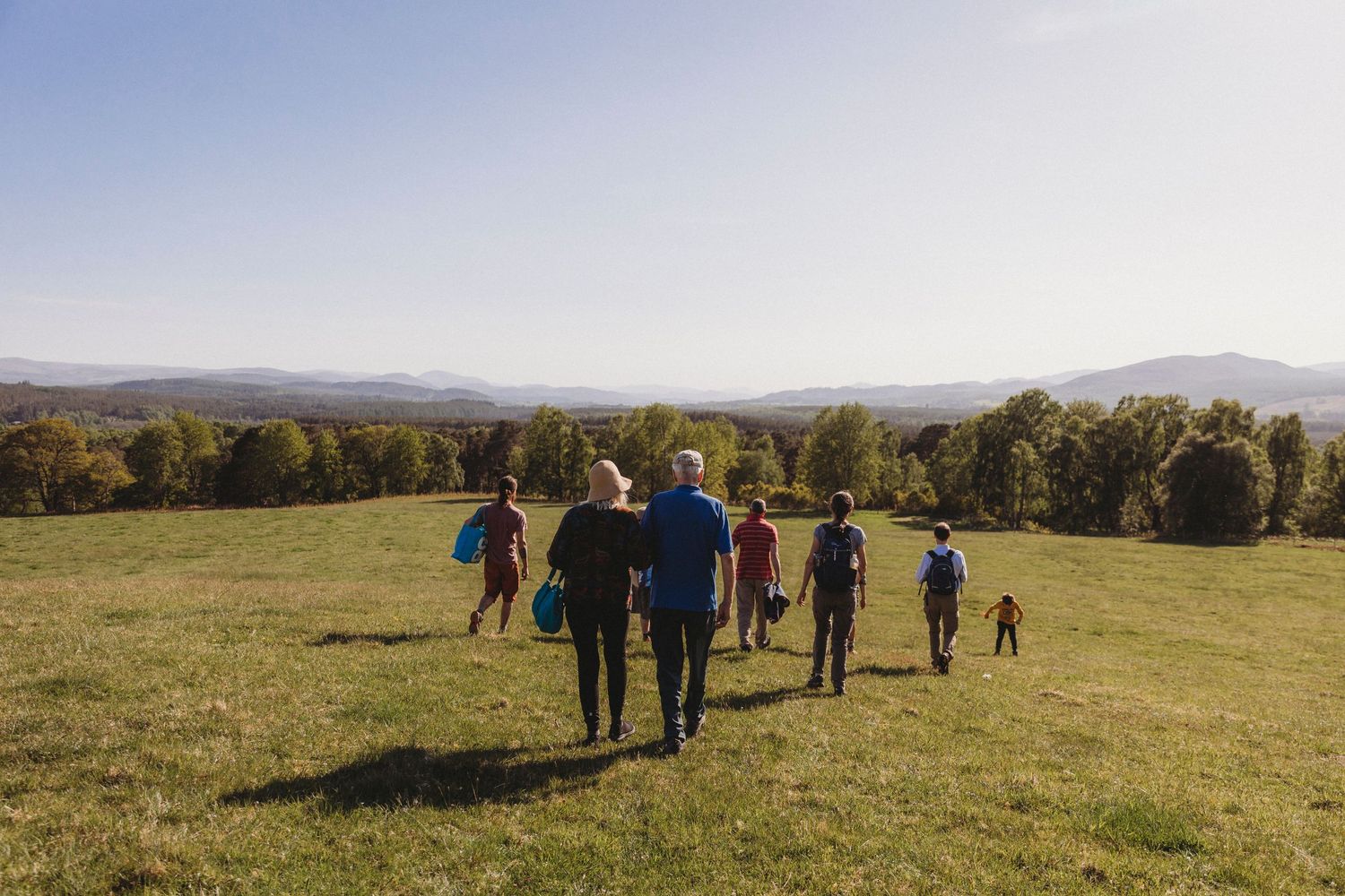 A group walks together across a scenic hilltop meadow with mountains in the distance.