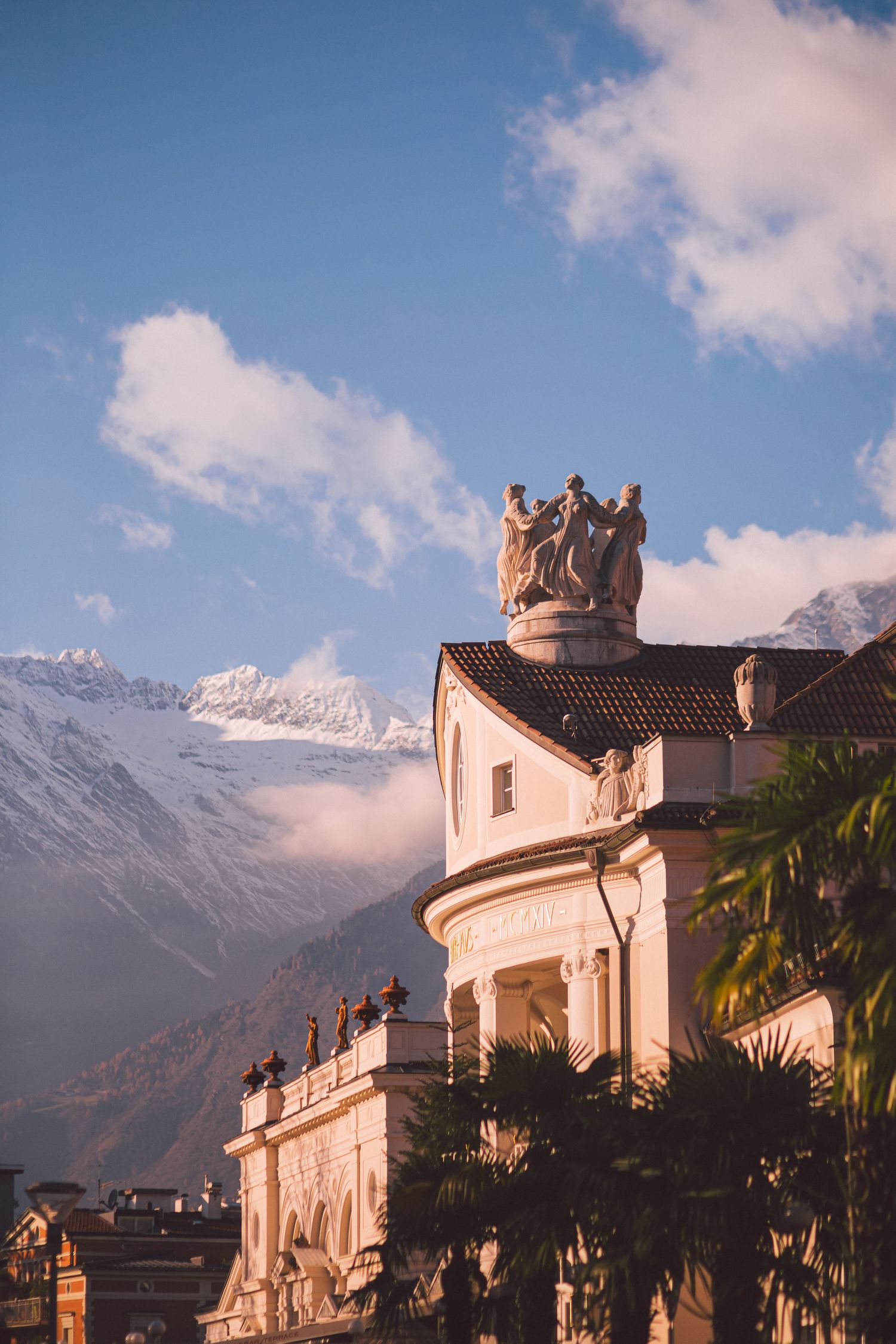 Ornate historical building with sculptural details against snow-capped mountain backdrop.