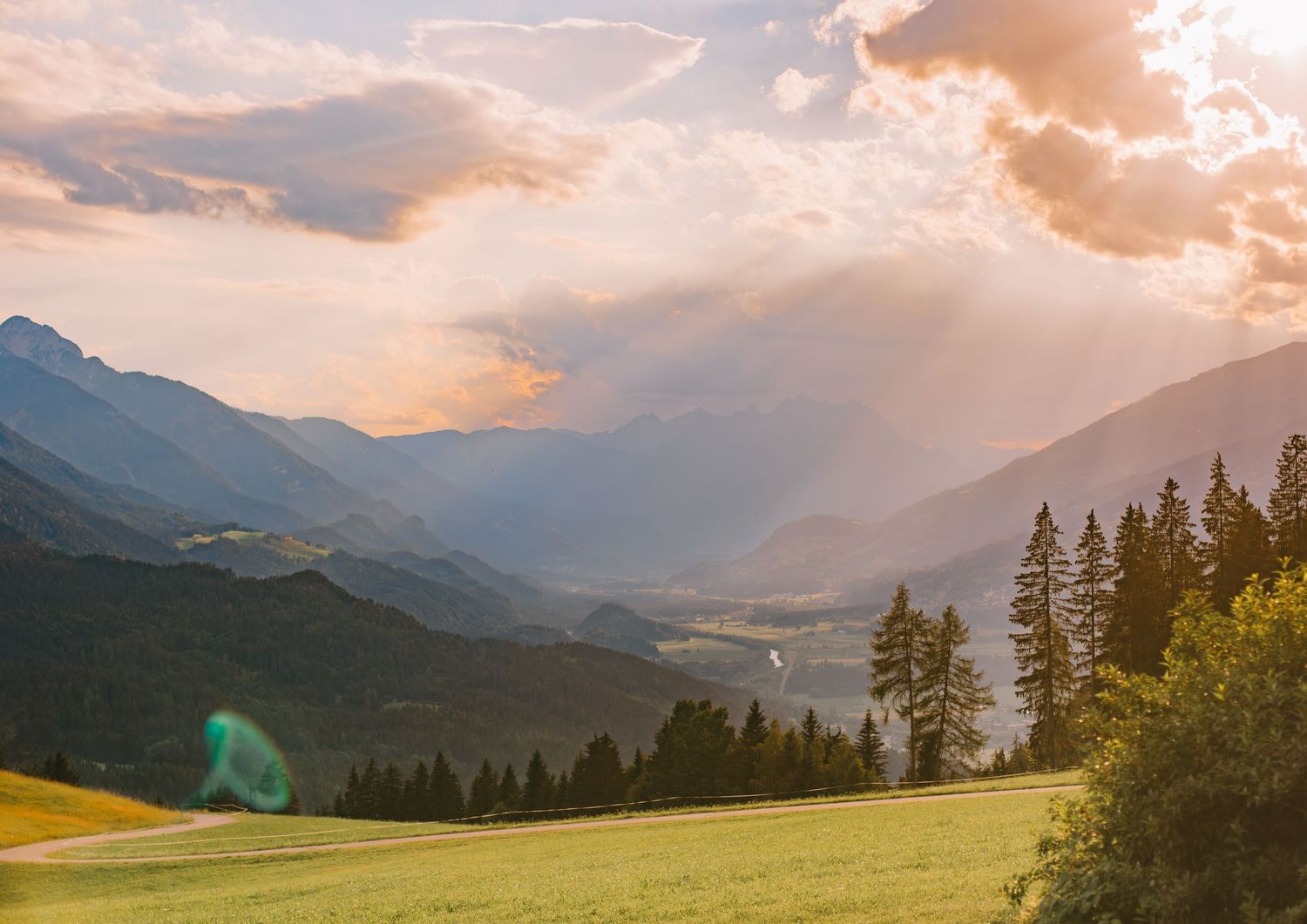 Scenic mountain landscape with sunbeams breaking through clouds over a forested valley.